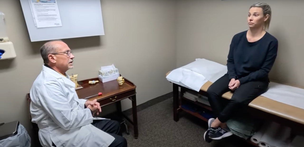 Dr. Geissele speaks with a female patient seated on an exam table during a consultation about sciatica